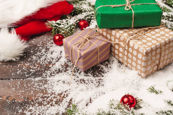 Presents on wooden background with fir tree branches and red baubles powdered with snow - 写真・画像