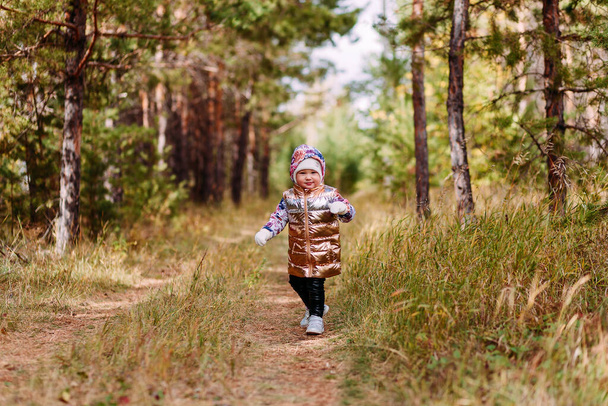 two-year-old girl in a golden vest walks in the forest in autumn - Foto, Imagem