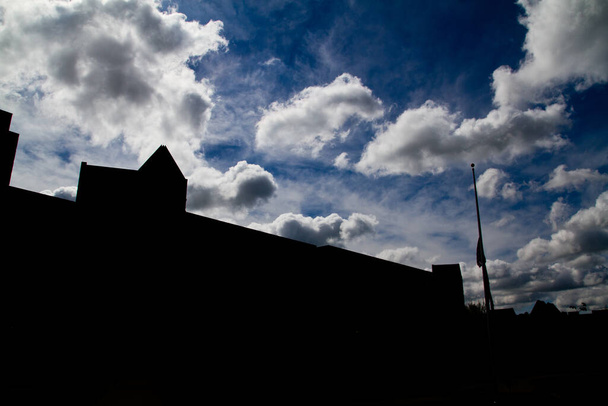 Suuret rakennukset ja lipputangon taustavalaistu ja siluetti vasten osittain pilvinen taivas - Valokuva, kuva