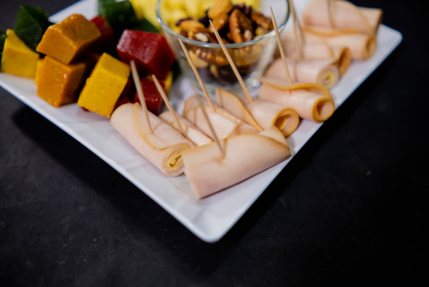 Rollos de jamón, pasta de frutas en cubitos, cubos de queso y nueces en un plato blanco cuadrado - Foto, Imagen