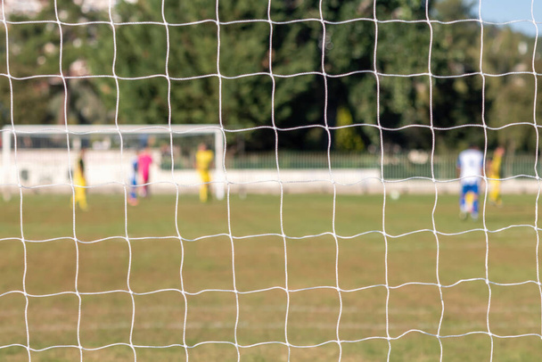 Football game in arena through soccer nets. Blurred players background - Photo, Image