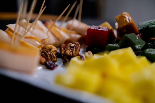 Πιάτο ρολό ζαμπόν, πάστα φρούτων, κύβους τυριού και ξηρούς καρπούς με θολή φόντο - Φωτογραφία, εικόνα