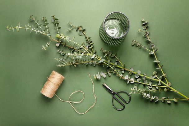 Composition with eucalyptus branch, glass vase, rope and scissors on color background - Photo, Image