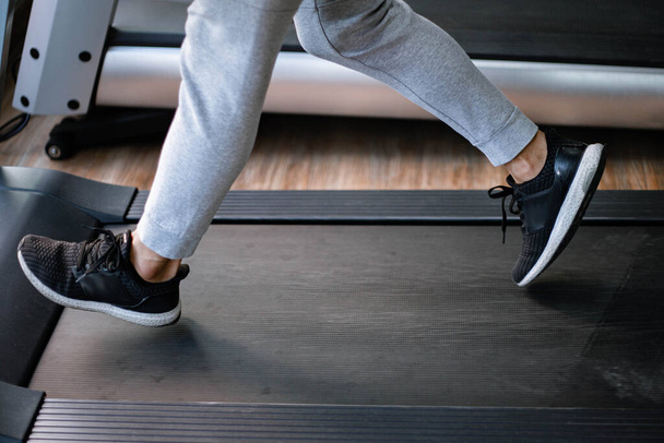 Training gym concept a male teenager wearing long pants and black trainers walking on a treadmill for cardio workout. - Fotografie, Obrázek