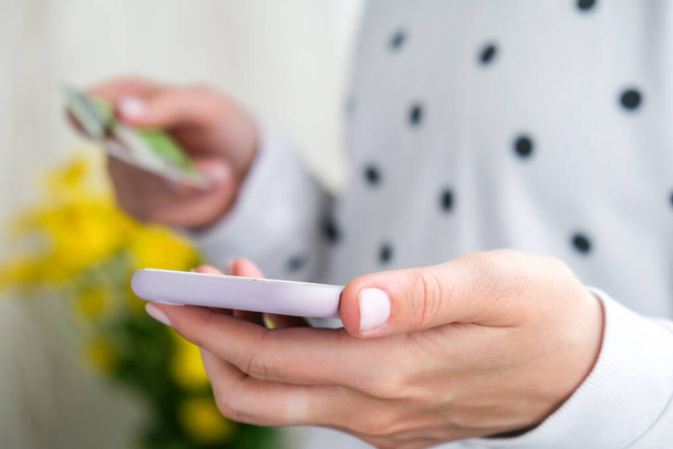 Close up view of female using online banking application on smartphone and holding debit credit card at home. Online shopping. Stay home - Photo, image