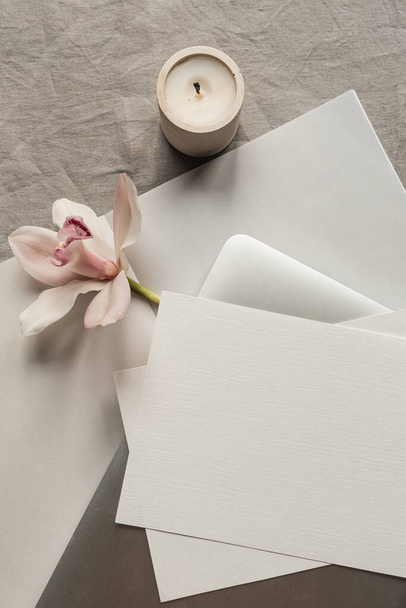 Aesthetic luxury bohemian minimalist concept. Blank paper sheet invitation card, laptop computer, pink flower, candle on neutral linen cloth. Flat lay, top view - Fotó, kép