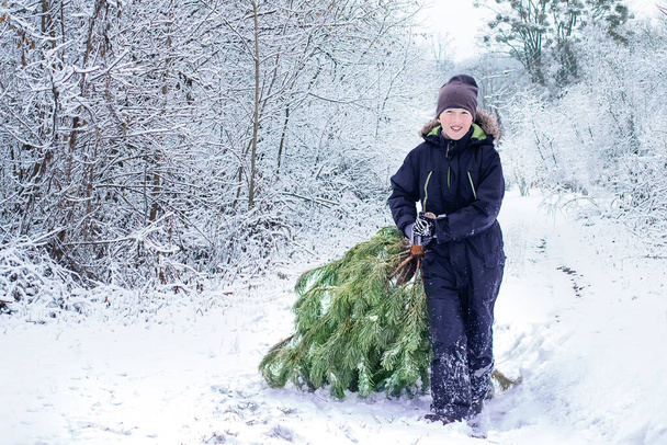 Семья, зимний отдых и понятие людей. Мальчик вытаскивает старую елку из леса в снегу к дому на рождественский вечер вдоль снежной дороги. Готовлюсь к Новому году. праздничный дух - Фото, изображение