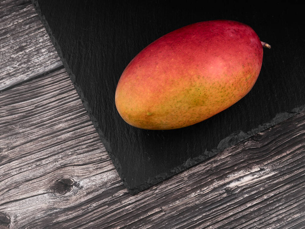 Frutas tropicales: Mango en una piedra negra sobre una mesa de madera - Foto, Imagen