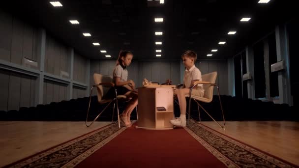 Écolier et fille s'assoient à la table d'échecs pendant un tournoi d'échecs rapide - Séquence, vidéo