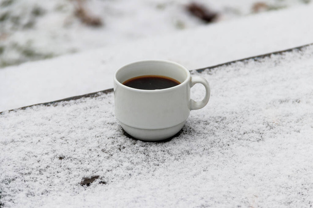 Kopje koffie op een met sneeuw bedekte tafel in de winter - Foto, afbeelding