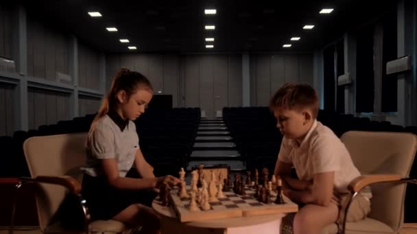 Молодая девушка пытается поставить мат своему сверстнику во время детского соревнования по быстрым шахматам - Кадры, видео