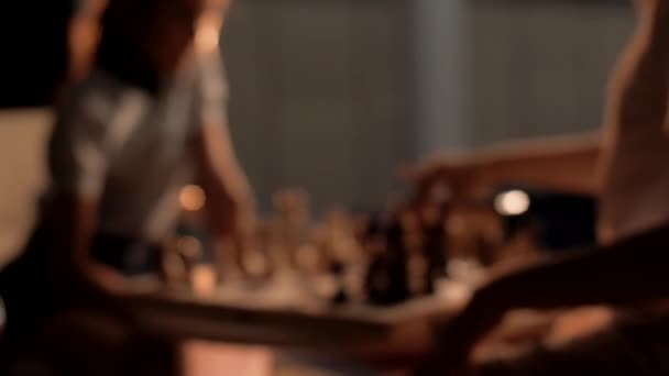 Ihmiset pelaavat shakkia pimeässä huoneessa lämpimällä valaistuksella. lähikuva - Materiaali, video