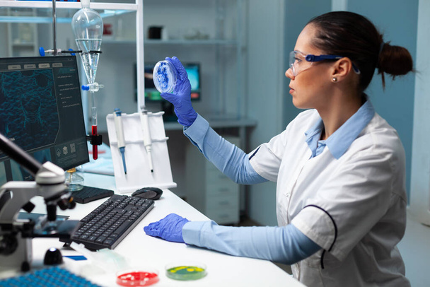 生物学者の女性は、青色溶液を分析透明ペトリ皿を保持 - 写真・画像