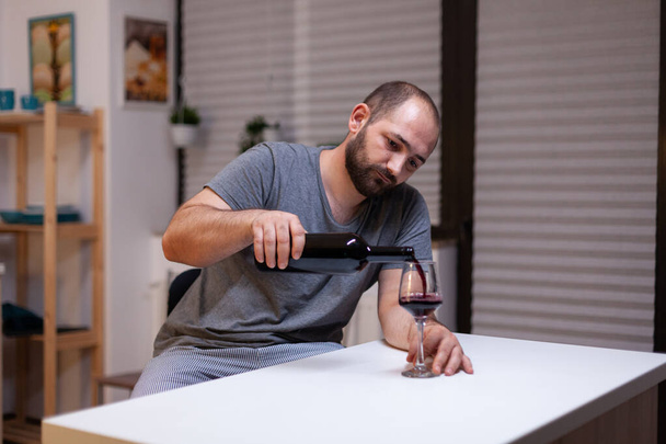 Μοναχικός άνθρωπος ρίχνει κρασί σε ποτήρι από μπουκάλι - Φωτογραφία, εικόνα