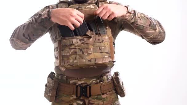 Egy férfi harci álruhában és testpáncélban puskagolyókat helyez a csomagtartóba a tányérhordozón. - Felvétel, videó