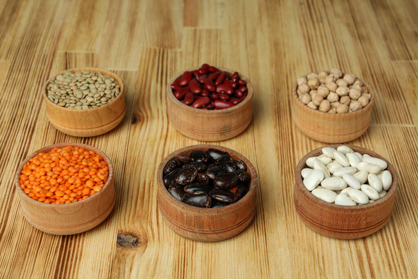 Mísy s různými druhy fazolí na dřevěném pozadí. - Fotografie, Obrázek
