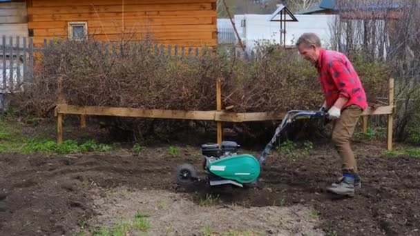 Hombre de edad avanzada araña el suelo con un cultivador o un bloque de labranza - Imágenes, Vídeo