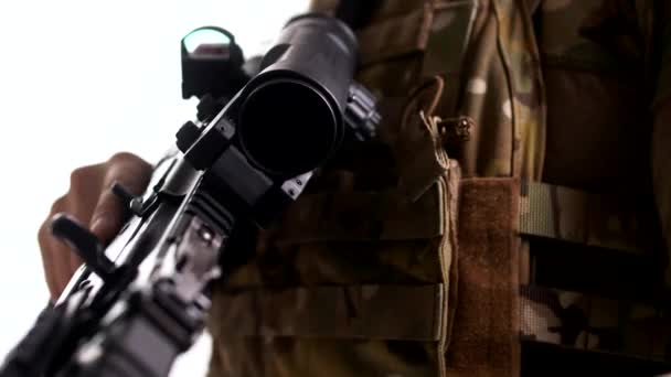 Modern harci puska teleszkópos látvánnyal és taktikai páncélzattal egy különleges alakulat katonája kezében. Közelkép, fehér háttér. Makró - Felvétel, videó