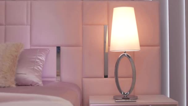 Moderna lámpara de noche cromada en un lujoso dormitorio junto a una cama elegante a la luz del sol de la mañana. Primer plano - Metraje, vídeo