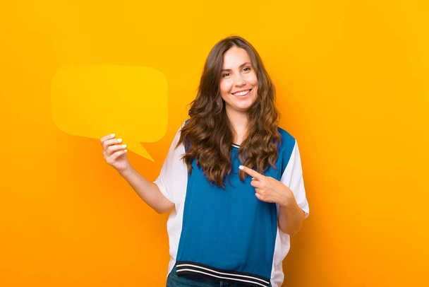 Female student pointing at the bubble speech she is holding over yellow background. - Фото, зображення