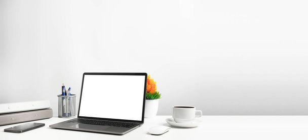 Ofisteki beyaz masadaki boş beyaz ekran dizüstü bilgisayar. Teknoloji akıllı telefonları, defter ve kahve fincanlarını kullanarak çalışıyor. Tasarım veya metin, Kapanış, Gri ve bulanık arkaplan için sağdaki boşluğu kopyala - Fotoğraf, Görsel