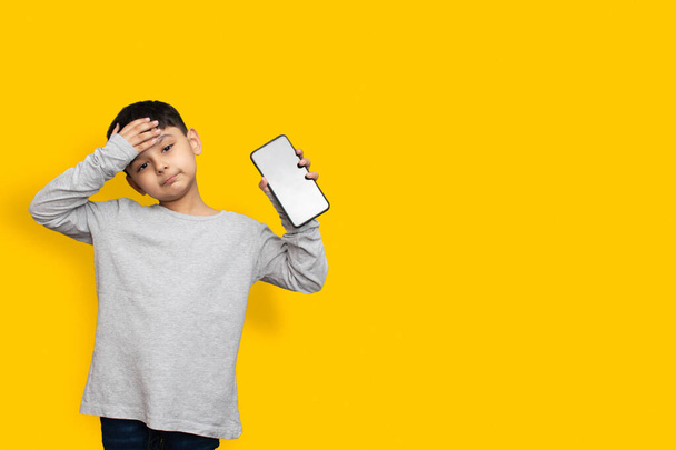 Улыбнись и потрясенный мальчик в зеленой серой рубашке пустой экран мобильного телефона на желтом фоне копировального пространства - Фото, изображение