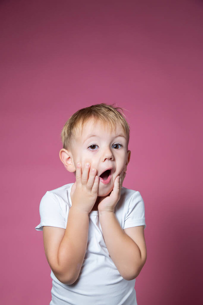Caucasian boy 3 years old makes scary faces while looking at the camera on a pink background - Фото, зображення