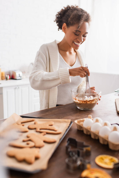 Boldog afro-amerikai nő főzés közelében elmosódott tojás és ízletes karácsonyi cookie-k a konyhában  - Fotó, kép