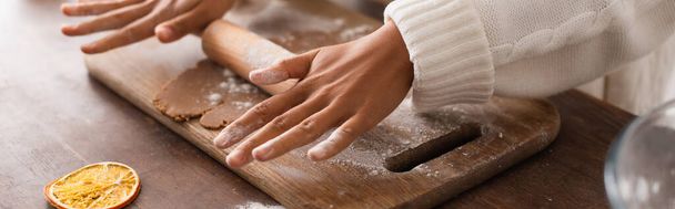 Cropped view of african american woman rolling dough near dry orange slice in kitchen, banner  - Photo, Image
