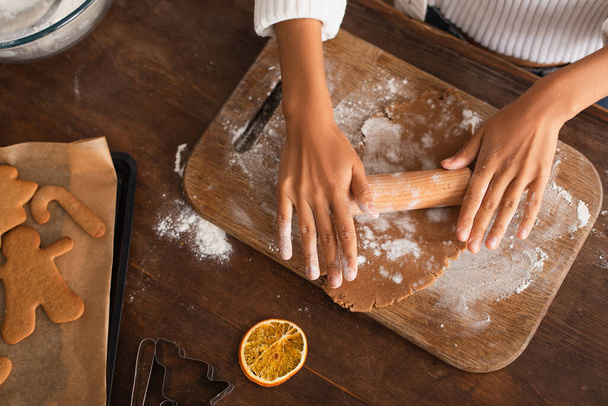 Cropped view of african american woman rolling dough near dry orange slice and christmas cookies in kitchen  - Photo, Image