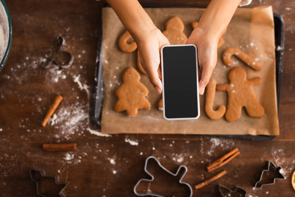 Vista superior de la mujer afroamericana tomando fotos en el teléfono inteligente cerca de las galletas borrosas de Navidad  - Foto, Imagen