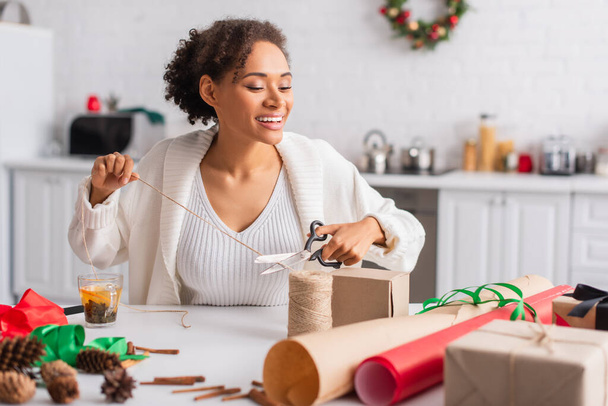 Femme afro-américaine positive coupe ficelle près du décor et des cadeaux à la maison  - Photo, image