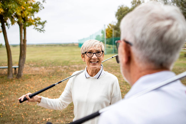 Aktywna para seniorów z kijami golfowymi ciesząca się wolnym czasem na świeżym powietrzu. - Zdjęcie, obraz
