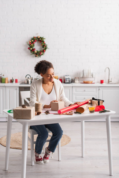 Usmívající se africká americká žena při pohledu na dárkové krabice a vánoční výzdoba doma  - Fotografie, Obrázek