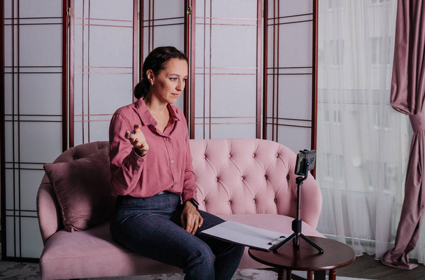 una psicologa donna con una camicetta rosa è seduta sul divano e conduce una consultazione online - Foto, immagini