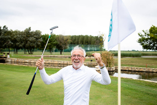 Portret van een actieve senior die het winnen op de golfbaan viert en geniet van vrije tijd buiten. - Foto, afbeelding