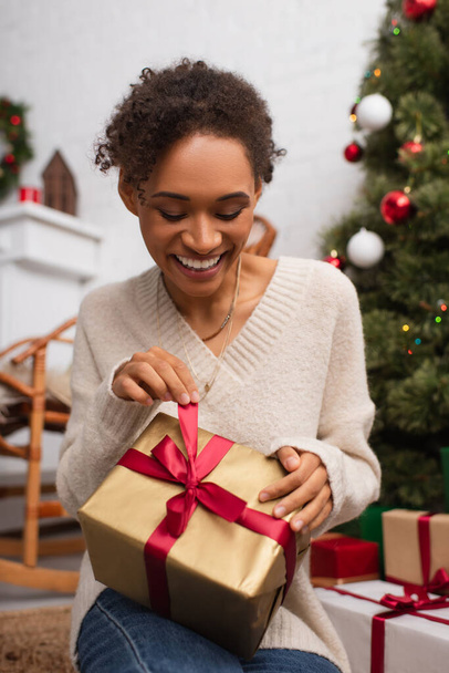 Evde Noel hediyesini çözerken gülümseyen genç Afrikalı Amerikalı kadın.  - Fotoğraf, Görsel