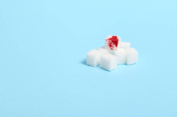 Всемирный день борьбы с диабетом, 14 ноября. Концепция, опасность поедания белого сахара. Чистые рафинированные кубики белого сахара с каплей крови, на синем фоне с копировальным местом для медицинской рекламы - Фото, изображение