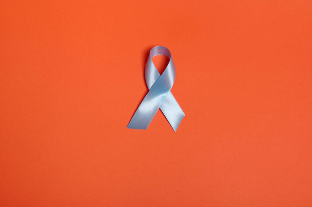Flat lay of a blue satin ribbon, symbolic bow color raising awareness in diabetes day on orange colored background with copy space for ad, 14 November. World diabetes day awareness concept. - Фото, зображення