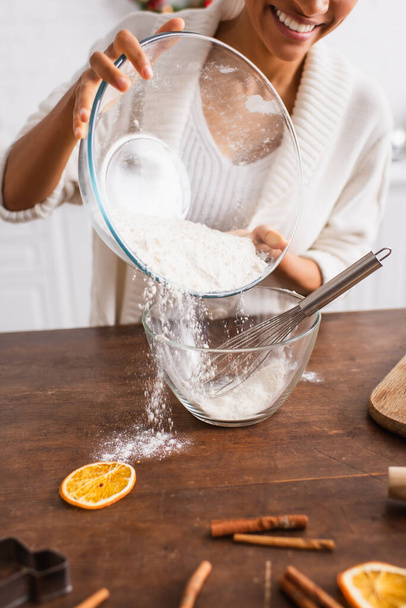 Cropped view of african american woman pouring flour near dry orange and blurred cinnamon sticks  - Foto, immagini