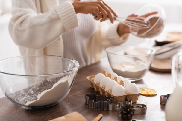 Vista cortada de ingredientes e cortadores de biscoitos perto de mulher afro-americana borrada cozinhar na cozinha  - Foto, Imagem