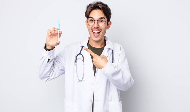 young hispanic man looking excited and surprised pointing to the side. doctor syringe concept - Foto, Imagem