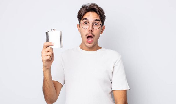 young hispanic man looking very shocked or surprised. alcohol flask concept - Фото, зображення