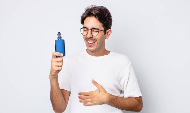 young hispanic man laughing out loud at some hilarious joke. smoke vaporizer concept - Foto, Imagen