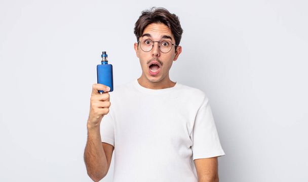 young hispanic man looking very shocked or surprised. smoke vaporizer concept - Фото, зображення