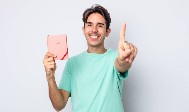 young hispanic man smiling proudly and confidently making number one. 2022 planner concept - Foto, immagini