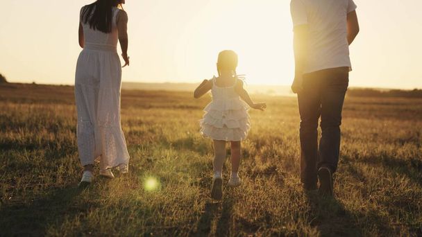 a little laughing girl runs with her parents at sunset, a happy family, a childhood dream, kid running in sunshine with mom and dad, playing catch-up with child, father and mother with baby daughter - 写真・画像