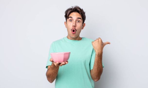 young hispanic man looking astonished in disbelief. empty bowl concept - Фото, изображение