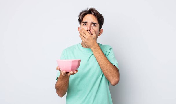young hispanic man covering mouth with hands with a shocked. empty bowl concept - Фото, зображення