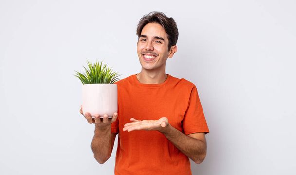young hispanic man smiling cheerfully, feeling happy and showing a concept. decorative plant concept - Foto, immagini